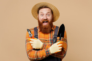 Happy surprised fun young bearded man wear straw hat overalls work in garden hold shovel gardening...