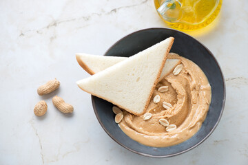 Bowl with peanut butter and bread slices for making sandwiches, horizontal shot on a light-beige marble background, high angle view