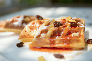 Waffles topped with honey and strawberry jam on a ceramic plate.