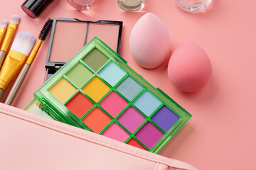 Bright summer eyeshadow palette and makeup products in pink cosmetic bag on pink background