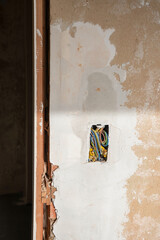 a bundle of multi-colored tangled wires in a hole in a peeling wall in house