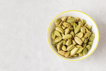 Aromatic condiment cardamom pods in white bowl isolated on light textured backdrop top view with copy space