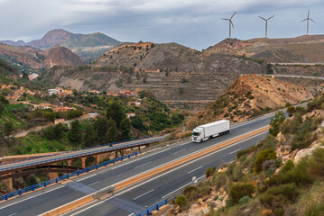 Truck with a refrigerated semi-trailer driving on a highway and a landscape with bridges,...