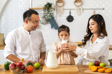 Portrait of enjoy happy love asian family father and mother with little asian girl smiling and having protein breakfast drinking and hold glasses of milk at table in kitchen