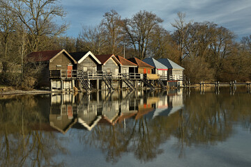 Fototapeta na wymiar Bootshäuser die am Strand im See stehen spiegeln sich im ruhigen Wasser.
