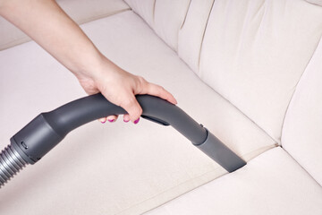 Close-up of a female hand vacuums the surface of the beige sofa - obrazy, fototapety, plakaty