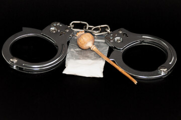 Handcuffs, a bag of white powder and handcuffs on a black background. Close-up. The concept of punishment for the manufacture and distribution of drugs.