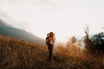 mother with children from behind, walk across a field among the mountains in the beautiful sunset...