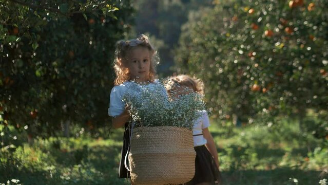 Little sisters carry white flowers in basket in the garden