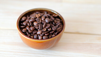 Fototapeta premium close-up of brown coffee beans in a bowl, coffee beans background, coffee beans in a bowl on wooden table, space for text, roasted coffee beans