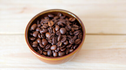 Fototapeta premium close-up of brown coffee beans in a bowl, coffee beans background, coffee beans in a bowl on wooden table, space for text, roasted coffee beans