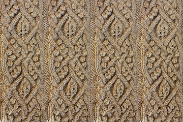 Beige background knitted fabric with a pattern. Knitted Arans close-up