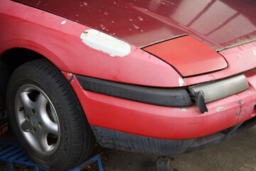 Rotes japanisches Auto der Neunzigerjahre mit Klappscheinwerfer und Lackschaden in einer Garage in...