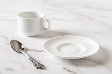Empty white plate, cup and spoon on a marble table. Clean porcelain crockery for food design mockup. Breakfast, eat and drink, tableware concept. High key image.