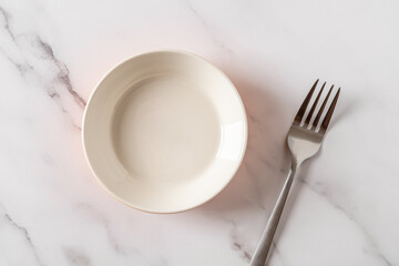 Orange ramekin and metal fork over white marble tabletop. Empty porcelain bowl for food design mockup. Modern ceramic crockery and tableware concept. High key image.