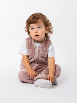 A curly-haired kid of 1-2 years old is sitting cross-legged on the floor in a sports plush suit, looking attentively at the top with his mouth open. Copy space. Photo.