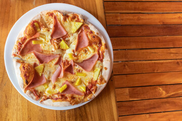 pizza hawaii with fresh pineapple and ham on a plate standing on a wooden table