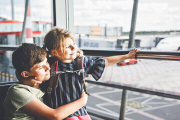Little girl and school boy at the airport waiting for boarding at big window. Two kids stands at...