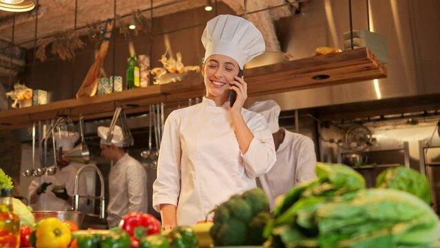 Portrait of professional famous female chef talking on phone before cooking tasty food. Attractive skillful woman working as cook ordering ingredients at modern fancy restaurant kitchen.