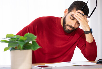 Stressed young man sitting at workdesk, touching his head