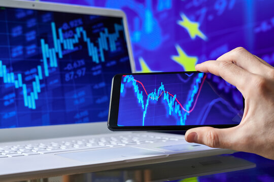 Trader analyzes stock market data in smartphone on the background of stock charts - Powered by Adobe