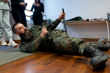 A bearded man in his 40s, a military medic lies on the floor and demonstrates to civilians in the...