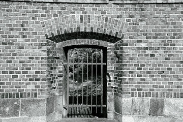 Metal grid in arched entrance of brick wall.Black and white photo.