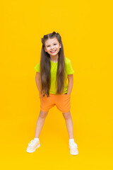 Fototapeta na wymiar A child in shorts and a T-shirt. Happy childhood. A little girl with long hair enjoys the warmth in summer clothes on a yellow isolated background.