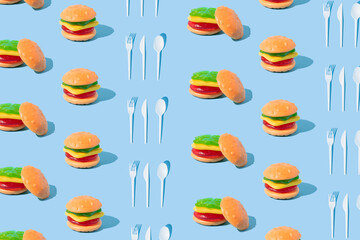 Hamburger shaped gummy candy and cutlery set with sunlight shadows on blue background. Food pattern.