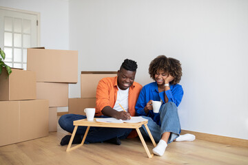 Black Couple Making List Of Necessities And Drinking Coffee After Moving Home