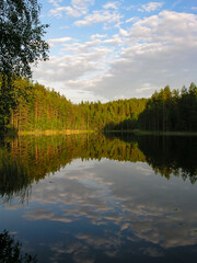 A tranquil lake in the woods with clouds reflected on the surface