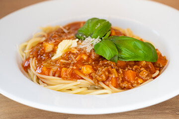homemade spaghetti bolognese with minced meat with juicy green basil, parmesan cheese, carrot pieces and butter shavings
