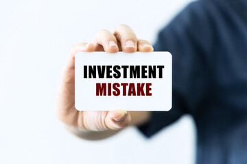Investment mistake text on blank business card being held by a woman's hand with blurred background. Business concept about mistakes when invseting.