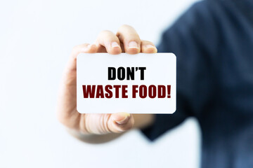 Don't waste food text on blank business card being held by a woman's hand with blurred background. Business concept about don't waste food.