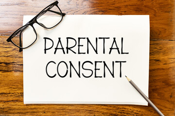 Parental consent text on blank notebook paper on wooden table with pencil and glasses aside. Business concept and legal concept about parental consent.