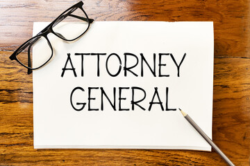 Attorney general text on blank notebook paper on wooden table with pencil and glasses aside. Business concept and legal concept about attorney general.