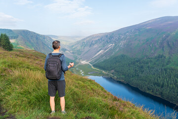 Hiker on the top of the mountain having coffee, on a summer day, and enjoying the a lake view.  The Spinc peak above Glenealo Valley in Glendalough, Wicklow, Ireland.