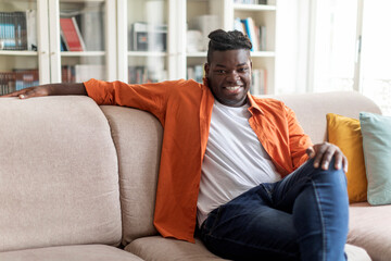 Relaxed cheerful black guy chilling on couch at home