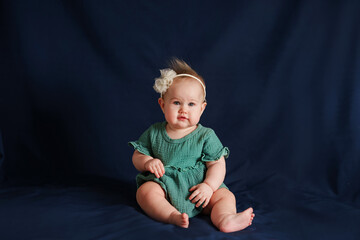 Fototapeta premium Portrait of a beautiful Caucasian baby toddler girl with a bow and muslin dress on a blue background