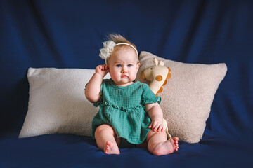 Portrait of a beautiful Caucasian baby toddler girl with a bow and muslin dress on a blue background