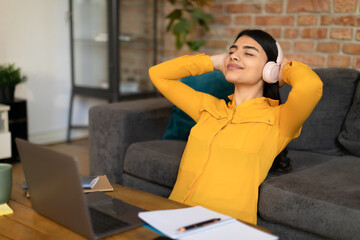 Relaxed spanish teenager lady listening to music online, wearing wireless headphones, taking break from study