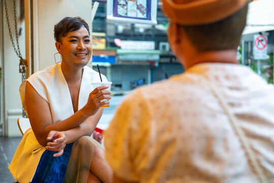Two Asian drag queen gay friends in woman clothes meeting and drinking coffee together at coffee shop in the city. Diversity sexual equality, lgbtq pride people and transgender cross-dressing concept.