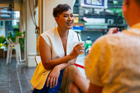 Two Asian drag queen gay friends in woman clothes meeting and drinking coffee together at coffee shop in the city. Diversity sexual equality, lgbtq pride people and transgender cross-dressing concept.