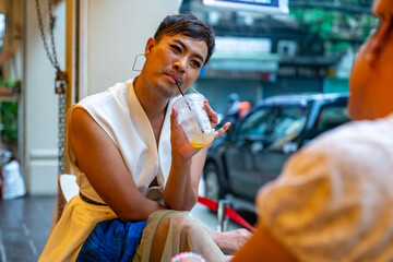 Two Asian drag queen gay friends in woman clothes meeting and drinking coffee together at coffee shop in the city. Diversity sexual equality, lgbtq pride people and transgender cross-dressing concept.