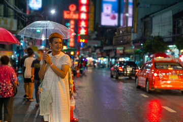 Happy Asian guy drag queen in woman clothes and makeup holding umbrella walking down city street in raining night. Diversity sexual equality, lgbtq pride people and transgender cross-dressing concept.