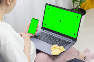 Pregnant girl looking into laptop and phone with empty green screen mockup