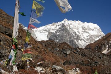 Montañas nevadas de fondo en una sendero por el valle de Langtang, Nepal, con banderas nepalís de oración de colores ondeando al viento.
