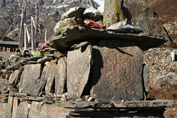 Piedras con rezos budistas grabados en el camino de ascenso por el valle de Langtang, Nepal, entre montañas de roca y banderas de colores de oración.