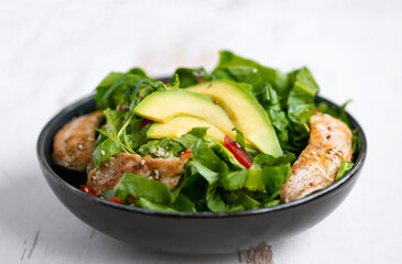 Healthy  vegetable buddha bowl salad with fried chicken and avocado, peppers and leaf lettuce on a white plate.