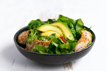 Healthy  vegetable buddha bowl salad with fried chicken and avocado, peppers and leaf lettuce on a white plate.